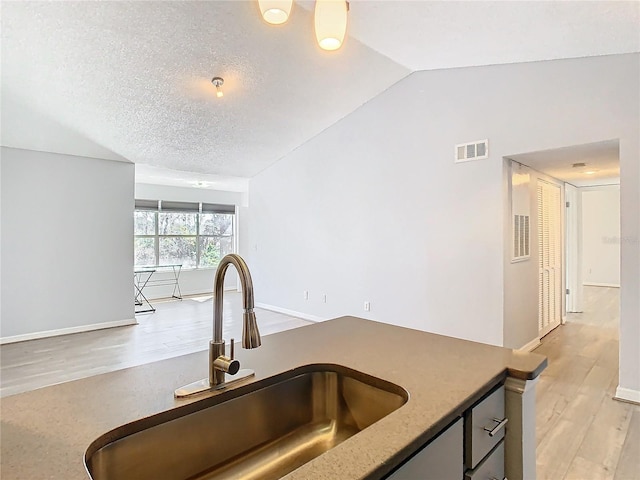 kitchen featuring lofted ceiling, sink, a textured ceiling, and light hardwood / wood-style flooring