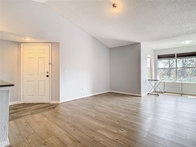 unfurnished living room with lofted ceiling, light hardwood / wood-style floors, and a textured ceiling