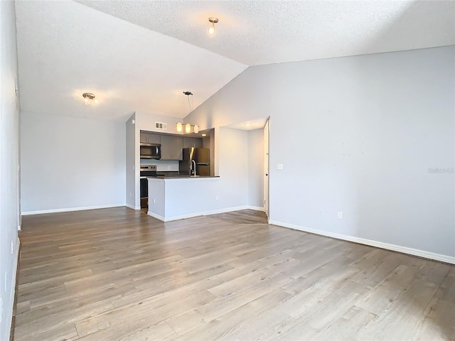 unfurnished living room featuring vaulted ceiling, a textured ceiling, and light wood-type flooring