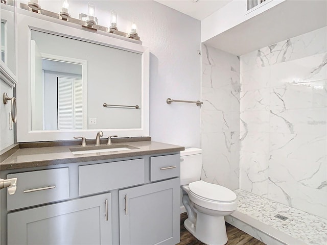 bathroom with vanity, wood-type flooring, tiled shower, and toilet