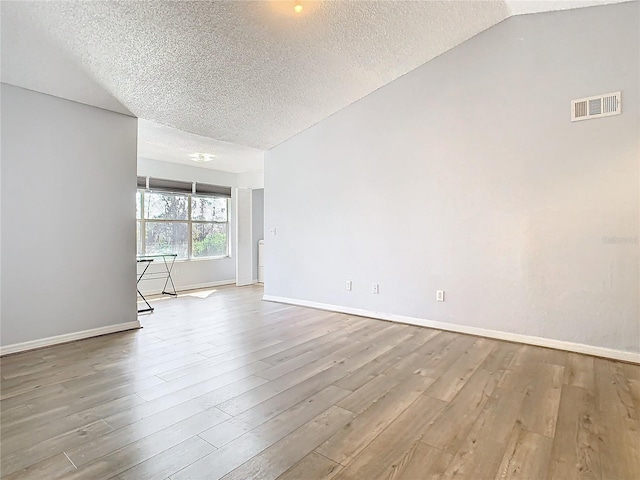 spare room with hardwood / wood-style floors, vaulted ceiling, and a textured ceiling