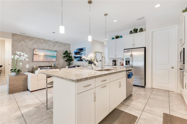 kitchen with pendant lighting, sink, white cabinetry, stainless steel appliances, and a center island with sink