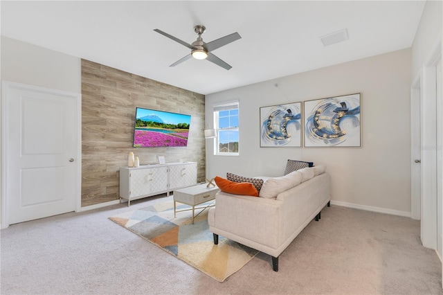 carpeted living room with ceiling fan and wood walls