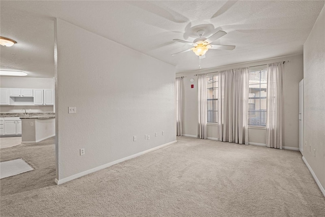 carpeted empty room with ceiling fan, sink, and a textured ceiling