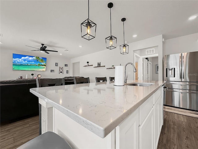 kitchen featuring sink, stainless steel fridge, an island with sink, pendant lighting, and light stone countertops