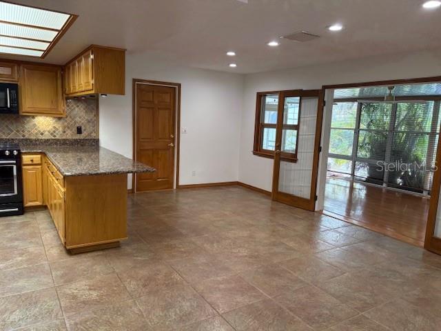 kitchen featuring stove, backsplash, dark stone countertops, a skylight, and kitchen peninsula