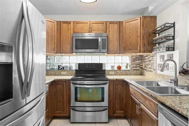 kitchen featuring sink, appliances with stainless steel finishes, tasteful backsplash, light stone counters, and a textured ceiling