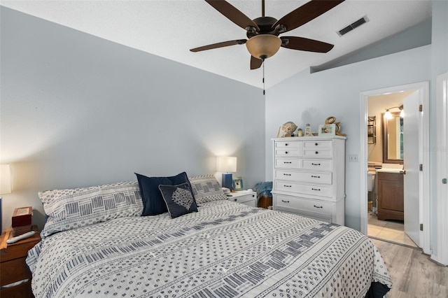 bedroom with vaulted ceiling, ceiling fan, light wood-type flooring, and ensuite bath