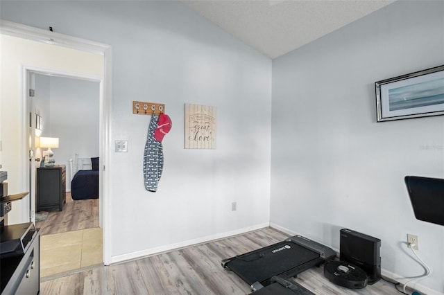 exercise room with lofted ceiling, light hardwood / wood-style floors, and a textured ceiling