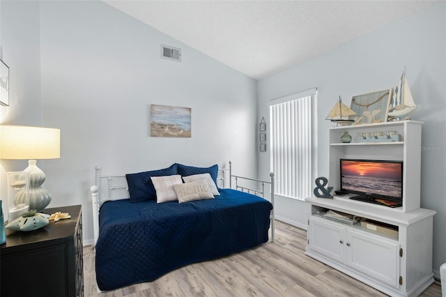 bedroom featuring lofted ceiling, a textured ceiling, and light wood-type flooring