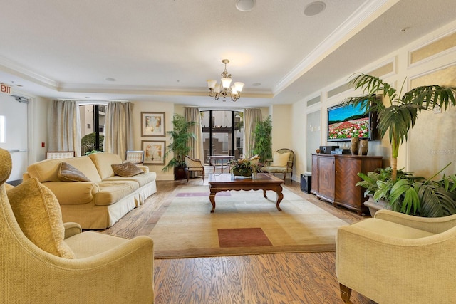 living room featuring a raised ceiling, ornamental molding, hardwood / wood-style flooring, and a notable chandelier