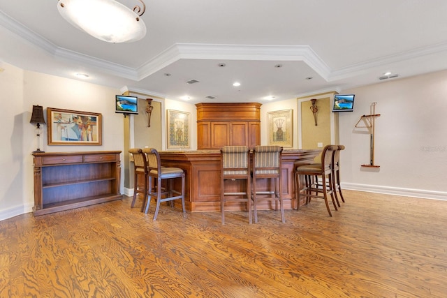 bar with ornamental molding, light wood-type flooring, and a tray ceiling