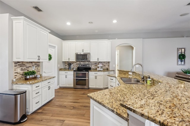 kitchen with sink, white cabinets, light stone counters, stainless steel appliances, and light wood-type flooring