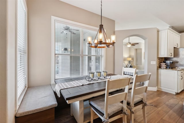 dining space with ceiling fan with notable chandelier and light hardwood / wood-style flooring