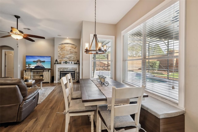 dining space featuring dark hardwood / wood-style flooring, ceiling fan with notable chandelier, and a fireplace