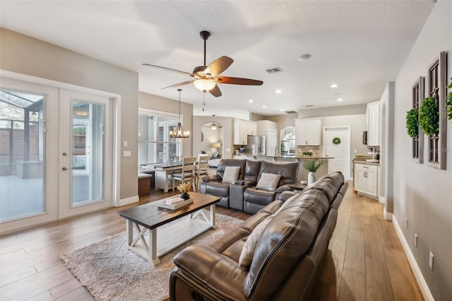 living room with ceiling fan with notable chandelier, french doors, a healthy amount of sunlight, and light wood-type flooring