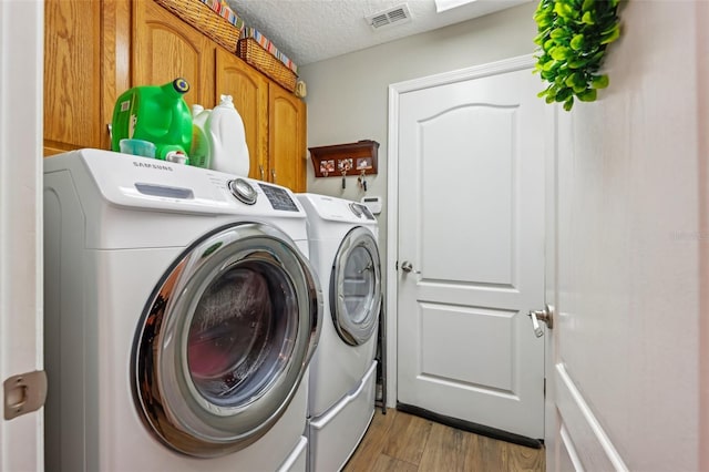 washroom with cabinets, separate washer and dryer, a textured ceiling, and light hardwood / wood-style flooring