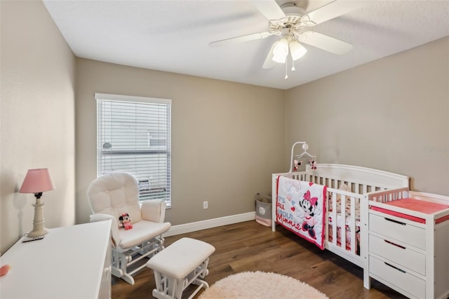 bedroom with a crib, dark hardwood / wood-style floors, and ceiling fan