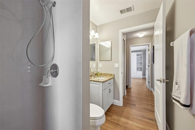 bathroom with hardwood / wood-style flooring, vanity, a shower, a textured ceiling, and toilet