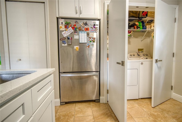 kitchen with sink, white cabinetry, separate washer and dryer, stainless steel fridge, and light stone countertops