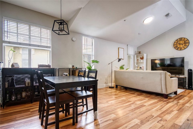 dining room with light wood-type flooring, visible vents, vaulted ceiling, and baseboards