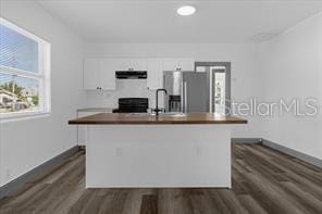 kitchen with range with electric cooktop, ventilation hood, an island with sink, white cabinets, and stainless steel fridge with ice dispenser