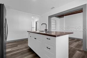 kitchen with dark wood-type flooring, sink, white cabinetry, stainless steel fridge, and a kitchen island