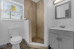 bathroom featuring hardwood / wood-style flooring, vanity, tiled shower, and toilet