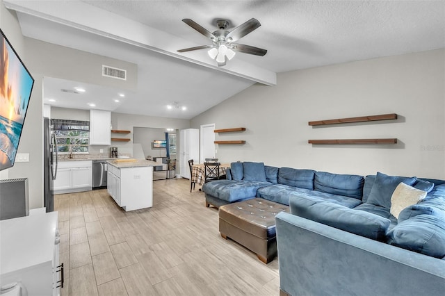 living room featuring vaulted ceiling with beams, sink, light wood-type flooring, ceiling fan, and a textured ceiling