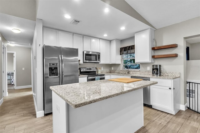 kitchen featuring sink, appliances with stainless steel finishes, white cabinetry, a center island, and light stone counters