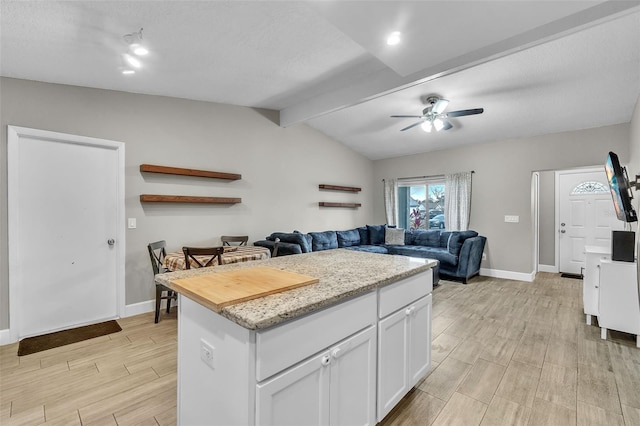 kitchen with white cabinetry, vaulted ceiling with beams, a center island, ceiling fan, and a textured ceiling