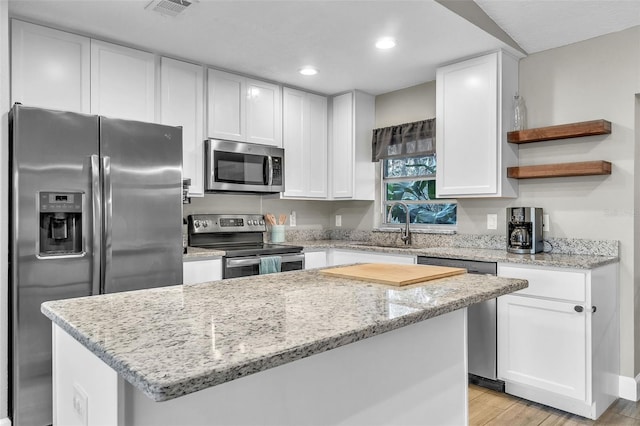 kitchen with a kitchen island, appliances with stainless steel finishes, sink, white cabinets, and light stone counters