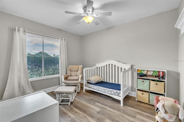 bedroom with hardwood / wood-style flooring, a crib, and ceiling fan