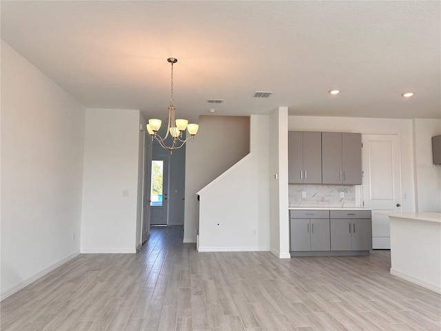 kitchen with tasteful backsplash, pendant lighting, light hardwood / wood-style floors, and an inviting chandelier