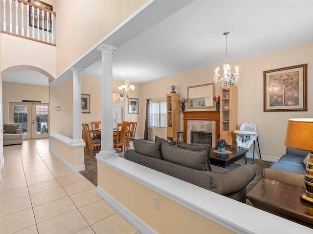 tiled living room with decorative columns, a tile fireplace, a healthy amount of sunlight, and an inviting chandelier