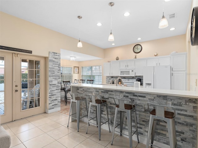 kitchen with light tile patterned floors, white appliances, white cabinetry, a kitchen breakfast bar, and decorative light fixtures