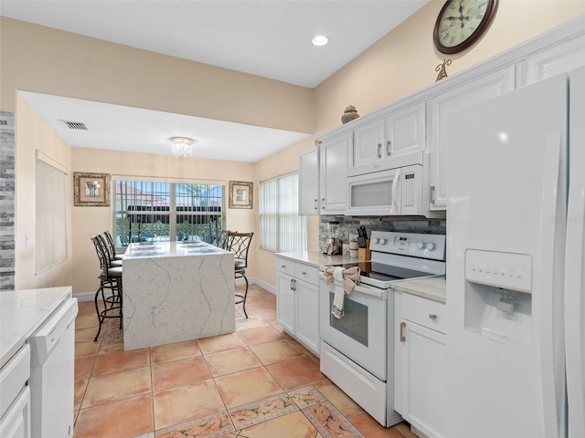 kitchen with light tile patterned floors, white appliances, white cabinetry, light stone countertops, and decorative backsplash