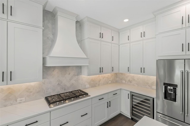 kitchen featuring appliances with stainless steel finishes, tasteful backsplash, white cabinets, wine cooler, and custom range hood