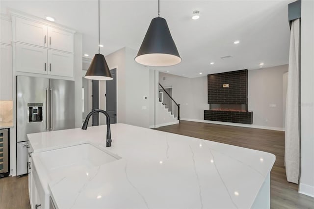 kitchen featuring pendant lighting, a large island, sink, white cabinetry, and light stone counters