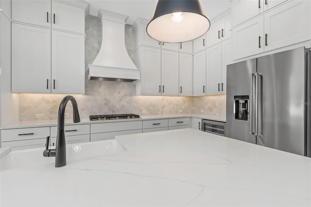 kitchen featuring backsplash, stainless steel appliances, light stone counters, white cabinets, and custom exhaust hood