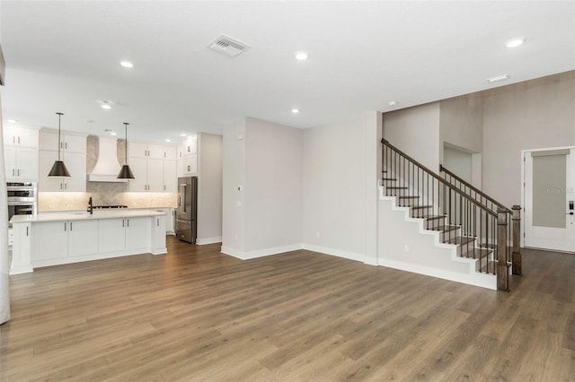 kitchen featuring appliances with stainless steel finishes, decorative light fixtures, an island with sink, white cabinets, and custom exhaust hood