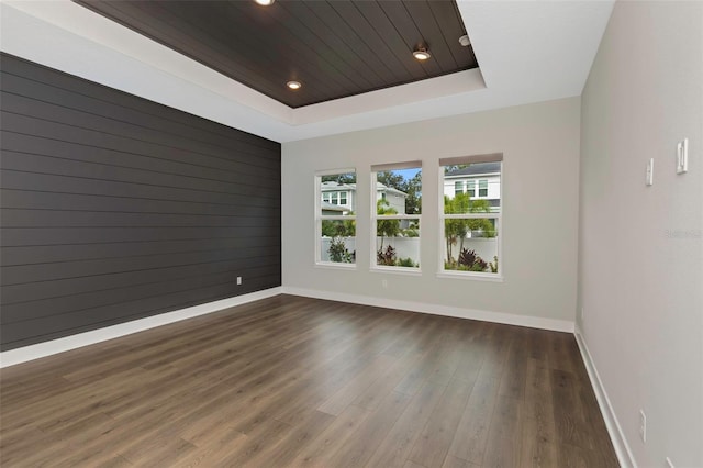 empty room featuring a raised ceiling, dark hardwood / wood-style floors, wooden ceiling, and wood walls