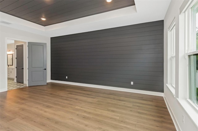 spare room with wooden walls, wood ceiling, light hardwood / wood-style floors, and a tray ceiling