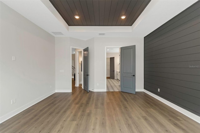 unfurnished bedroom featuring dark hardwood / wood-style flooring, wooden walls, and a raised ceiling