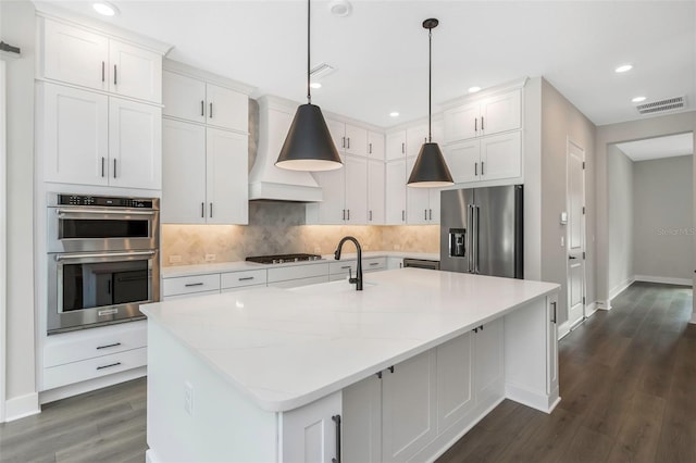 kitchen with premium range hood, appliances with stainless steel finishes, a kitchen island with sink, and white cabinets