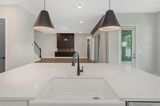 kitchen featuring hanging light fixtures, sink, a fireplace, and light stone counters