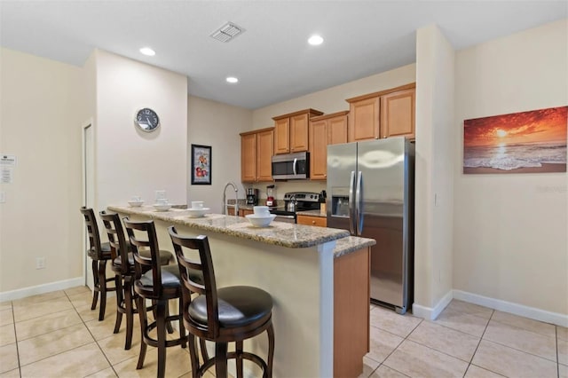 kitchen featuring a breakfast bar, light stone counters, light tile patterned floors, appliances with stainless steel finishes, and kitchen peninsula