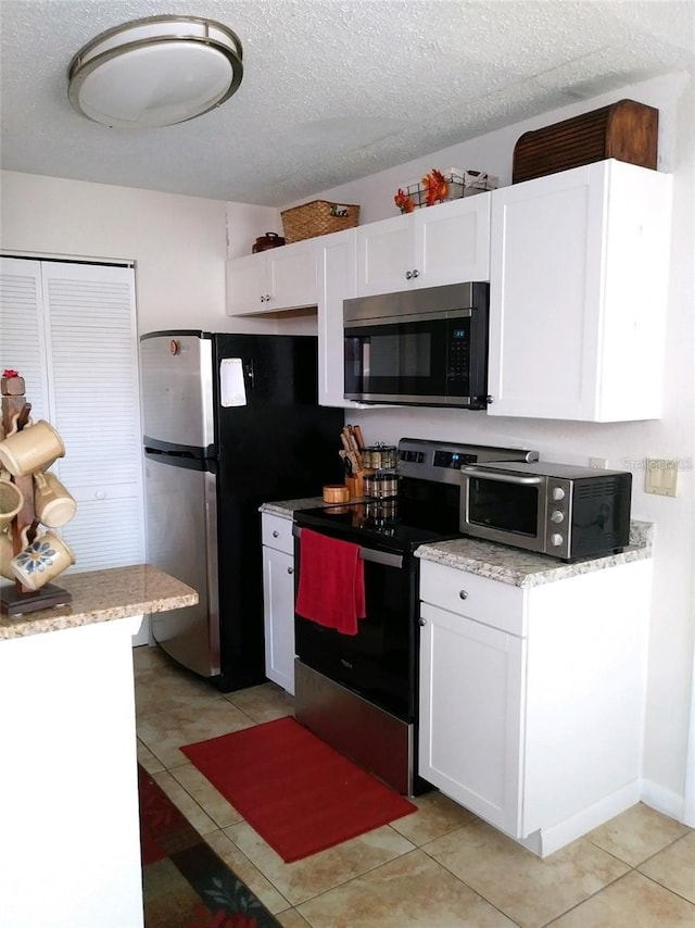 kitchen featuring light stone counters, a textured ceiling, light tile patterned floors, appliances with stainless steel finishes, and white cabinets