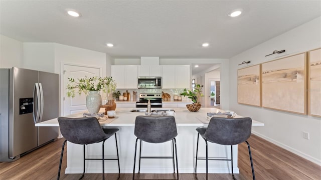 kitchen featuring hardwood / wood-style floors, stainless steel appliances, tasteful backsplash, an island with sink, and white cabinets