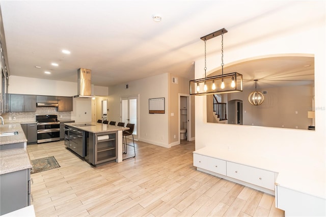 kitchen with decorative light fixtures, range with two ovens, island exhaust hood, a center island, and light stone countertops